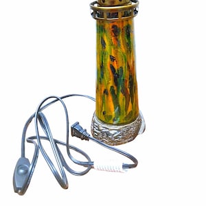 May include: A gold and green lighthouse-shaped electric lamp with a black cord and on/off switch. The lamp has a stained glass design with yellow, green, and black colors.