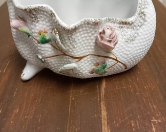 May include: A white ceramic bowl with a scalloped rim and three feet. The bowl is decorated with pink and green flowers and gold accents.