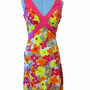Puede incluir: Vestido sin mangas con estampado floral y escote en V. El vestido presenta un corpi&ntilde;o rosa y una falda con un estampado de flores amarillas, naranjas y rosas. El vestido se exhibe en un maniqu&iacute;.