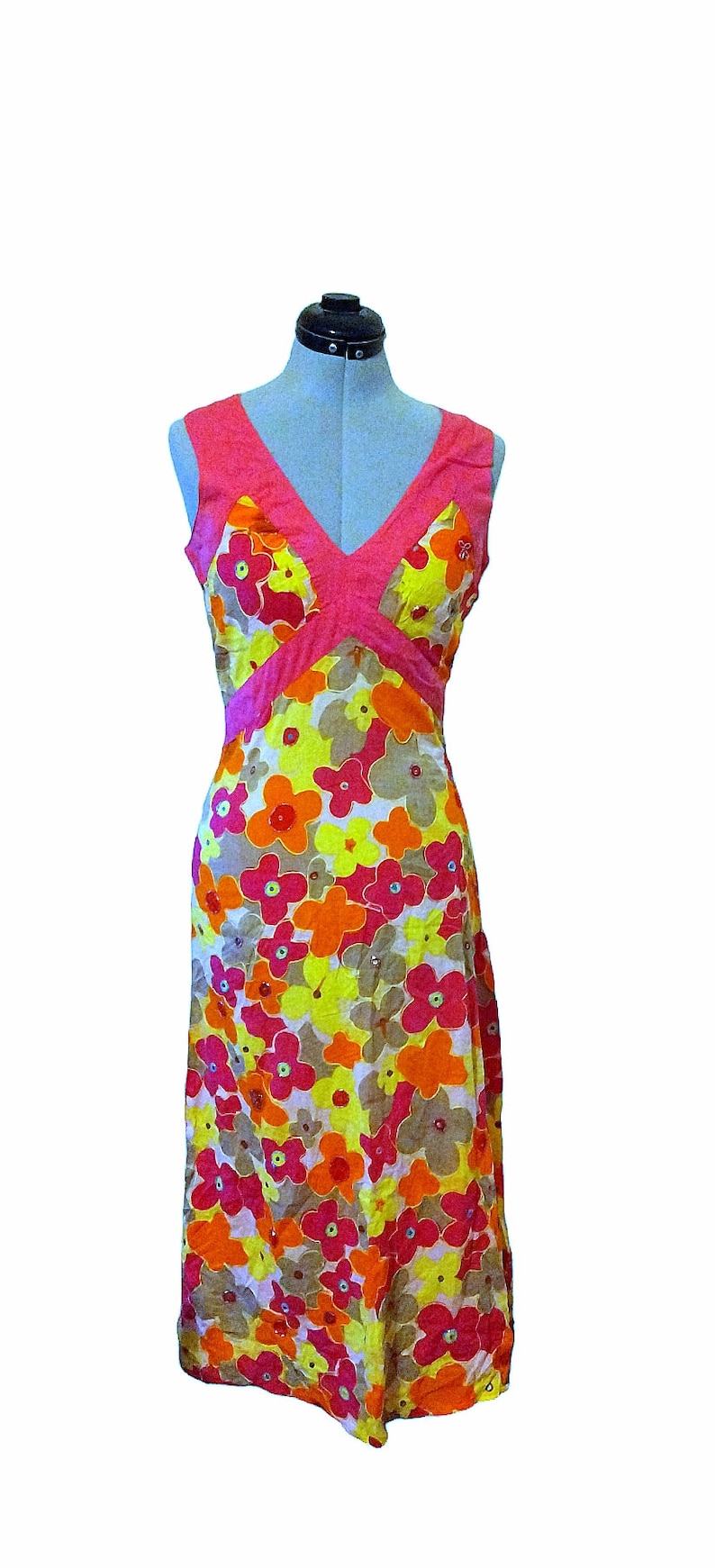 Puede incluir: Vestido sin mangas con estampado floral y escote en V. El vestido presenta un corpi&ntilde;o rosa y una falda con un estampado de flores amarillas, naranjas y rosas. El vestido se exhibe en un maniqu&iacute;.