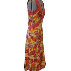 Puede incluir: Un vestido largo sin mangas con un estampado floral en tonos amarillos, naranjas, rosas y marrones. El vestido tiene un escote en V y ribetes rosas. El vestido se exhibe en un maniqu&iacute;.