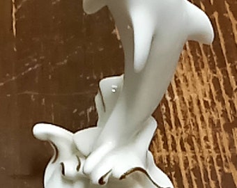 May include: White porcelain dolphin figurine with gold accents, leaping out of the water. The dolphin is positioned on a base with a wave design.