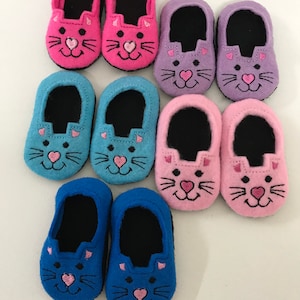 May include: Eight pairs of felt cat slippers in pink, purple, blue and light blue. Each slipper has a black felt lining and a cute embroidered cat face with pink details.