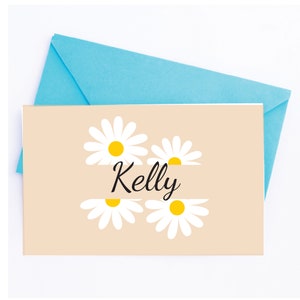 May include: A light brown card with a white daisy design and the name "Kelly" written in black cursive.