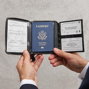 Può includere: Un portafoglio nero a tre ante con uno scomparto centrale che contiene un passaporto blu degli Stati Uniti. Il pannello sinistro mostra un modulo di certificato medico, mentre quello destro ha due scomparti per una licenza FAA.