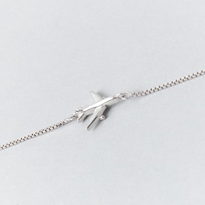 Peut inclure: Un bracelet en chaîne argent avec un petit pendentif avion.