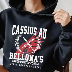 May include: Black hooded sweatshirt with the text "CASSIUS AU BELLONA'S RAZOR MASTER COURSE STEEL SHARPENS STEEL" in white. The design includes crossed swords and a laurel wreath in red and white.