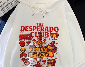 May include: White hoodie with a front graphic that reads "THE DESPERADO CLUB" with a dagger, skulls, and other illustrations. A black hoodie is next to it. The white hoodie has a front pocket and a drawstring hood.
