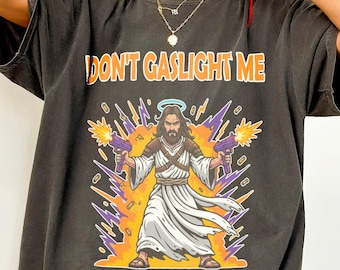 May include: Dark gray t-shirt with the text "DON'T GASLIGHT ME" above an illustration of Jesus holding two purple ray guns. The text "BLESSED BE THE BULLETS" is below the illustration.