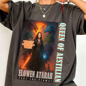 May include: Dark gray t-shirt featuring a fantasy graphic. The graphic includes a woman with dragons, a sword, and the text "QUEEN OF AESTILLIAN" and "ELOWEN ATARAH Fear the Flames".
