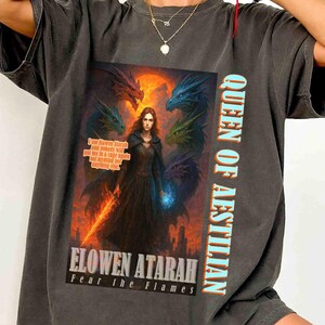 May include: Dark gray t-shirt featuring a fantasy graphic. The graphic includes a woman with dragons, a sword, and the text "QUEEN OF AESTILLIAN" and "ELOWEN ATARAH Fear the Flames".