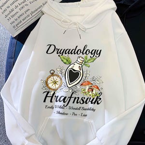 May include: White hoodie with the word "Dryadology" above a graphic of a potion bottle, compass, and mushrooms. Below the graphic is the word "Hrafnsvik" and the names "Emily Wilde - Wendell Bambleby - Shadow - Poe - Lisa". A black hoodie is next to it.