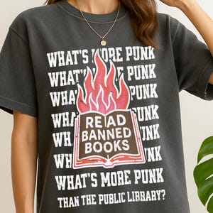 May include: Dark gray t-shirt with the text "WHAT'S MORE PUNK THAN THE PUBLIC LIBRARY?" and a graphic of a book with flames. The shirt's design includes the words "READ BANNED BOOKS".