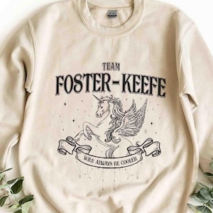 May include: A beige sweatshirt with a unicorn graphic and the text "Team Foster-Keefe Will Always Be Cooler".