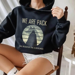 May include: Black hooded sweatshirt with the text "WE ARE PACK" above a circular graphic featuring a wolf silhouette and a cloaked figure. The text "THE REALM OF THE ELDERLINGS" is below the graphic.