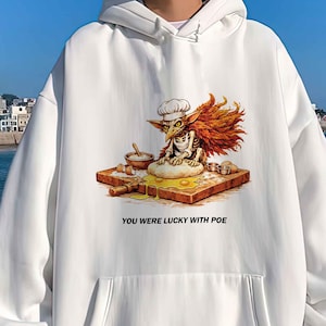 May include: White hoodie with a front pocket and a drawstring hood. The graphic on the front features a cartoon character wearing a chef's hat, with the text "YOU WERE LUCKY WITH POE" below the image.