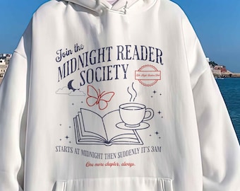 May include: White hooded sweatshirt with a front pocket and long sleeves. The sweatshirt features a graphic with the text "Join the MIDNIGHT READER SOCIETY" and illustrations of a book, butterfly, and coffee cup. The text "STARTS AT MIDNIGHT THEN SUDDENLY IT'S 3AM" is also included.