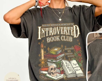 May include: A black t-shirt with a graphic print of a skull and books. The text on the shirt reads "Proudly Anti-Social Member of the Introverted Book Club".
