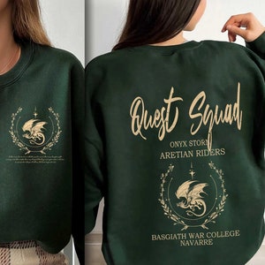 May include: A dark green sweatshirt with a gold dragon and floral design on the front and the text "Quest Squad" with the words "Onyx Storm", "Aretian Riders", "Basgiath War College", and "Navarre" on the back.