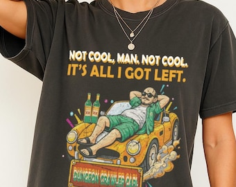 May include: Dark gray t-shirt with the text "NOT COOL, MAN, NOT COOL. IT'S ALL I GOT LEFT." A graphic depicts a man reclining in a yellow car with bottles and a sign that reads "Dungeon Crawler Park."