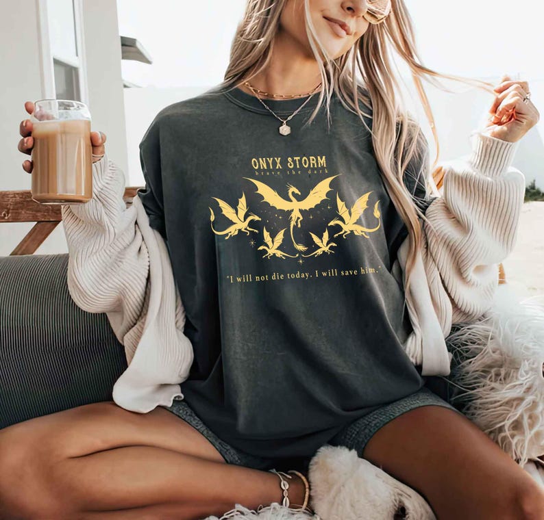 May include: A black long-sleeved shirt with a yellow graphic of a dragon and the text "ONYX STORM" and "Brave the Dark". The text "I will not die today. I will save him." is printed below the graphic.