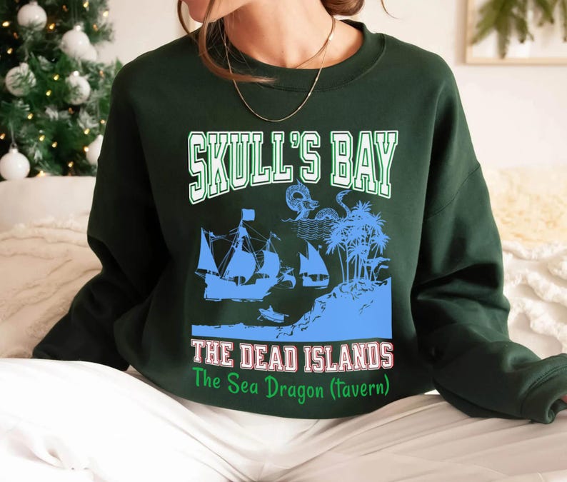 May include: Dark green sweatshirt with a graphic featuring the text "SKULL'S BAY" above a blue illustration of sailing ships and an island. Below the image, the text reads "THE DEAD ISLANDS" and "The Sea Dragon (Tavern)".