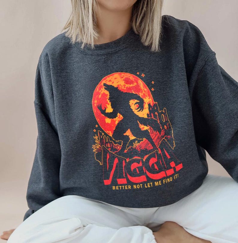 May include: Dark gray sweatshirt featuring a werewolf silhouette against a red moon. The design includes a castle and the text "VIGGA! BETTER NOT LET ME FIND IT!" in red and orange. A casual, spooky themed garment.