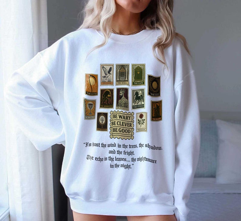 May include: White sweatshirt featuring a collection of vintage-style postage stamp illustrations in shades of brown, green, and gold. The text "BE WARY BE CLEVER BE GOOD" is printed below the stamps, with a quote below.