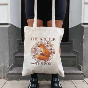 May include: A beige tote bag with a fox illustration and the text "The Archer The Fox".
