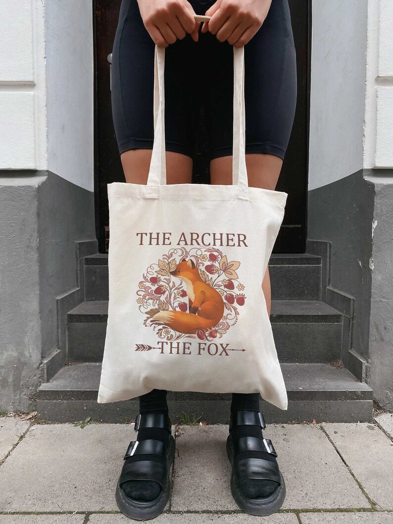 May include: A beige tote bag with a fox illustration and the text "The Archer The Fox".