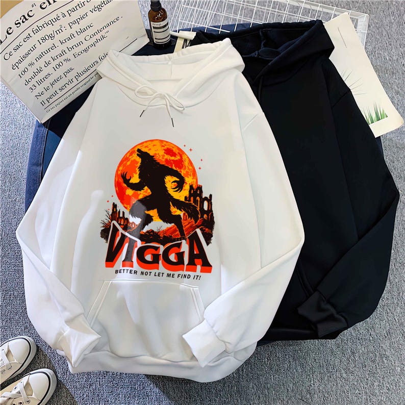 May include: White hoodie with a front graphic of a werewolf silhouette against a red moon and a castle. The word "VIGGA" is printed below the graphic in orange and black, with the text "BETTER NOT LET ME FIND IT!" below it. A black hoodie is next to it.
