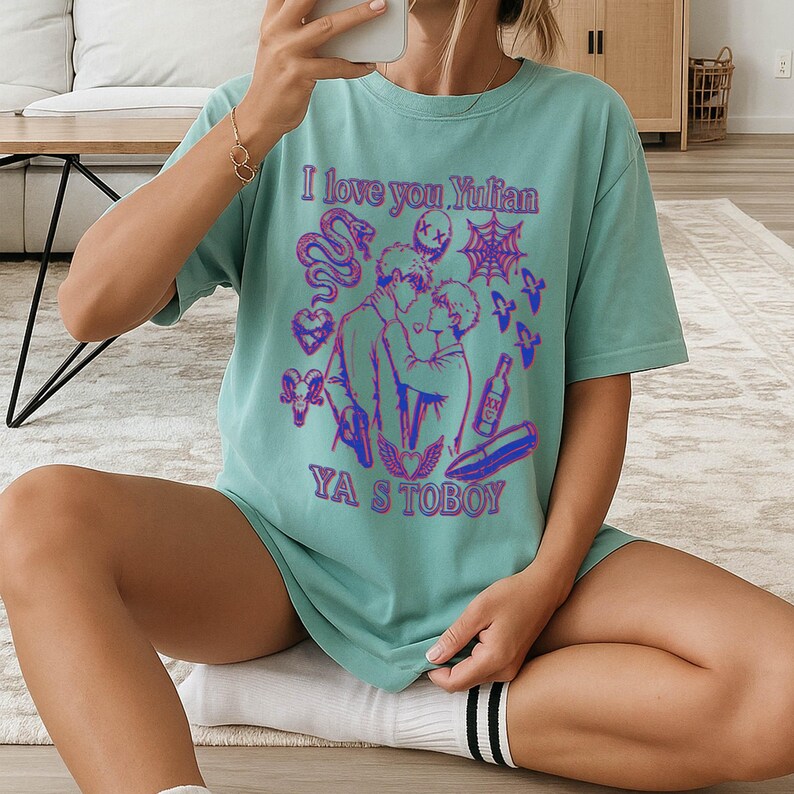May include: A light teal t-shirt with a graphic design featuring two figures kissing, a snake, hearts, and the text "I love you Yulian" and "YA S TOBOY" in purple and blue.