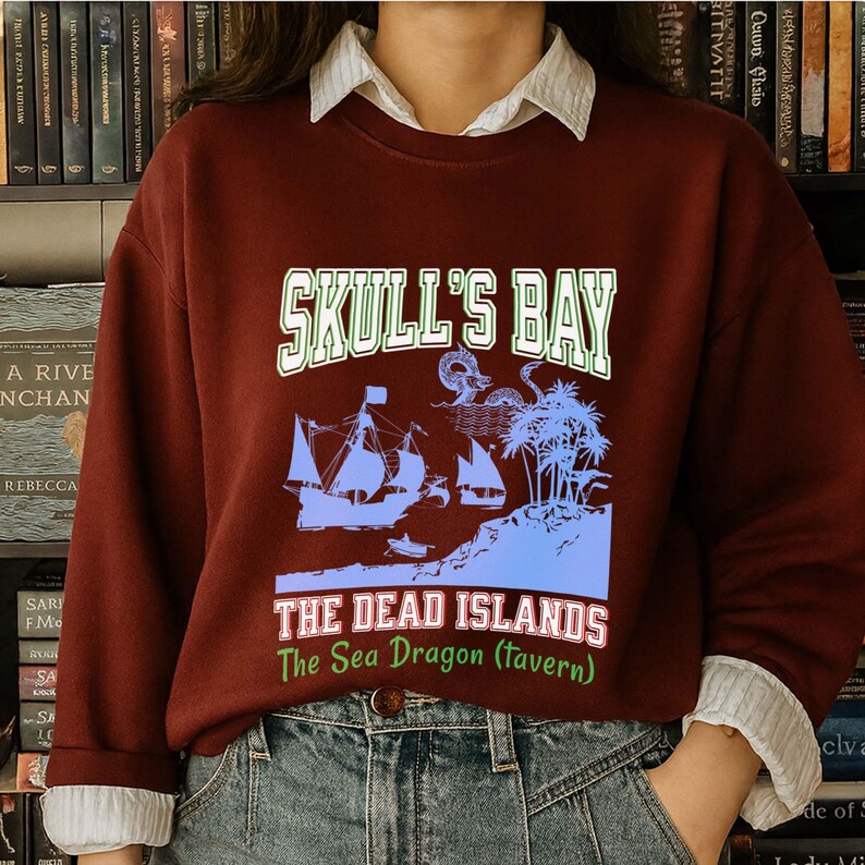 May include: A maroon sweatshirt with a graphic featuring a pirate ship, palm trees, and the text "SKULL'S BAY" and "THE DEAD ISLANDS The Sea Dragon (tavern)". The design is in shades of blue and green.