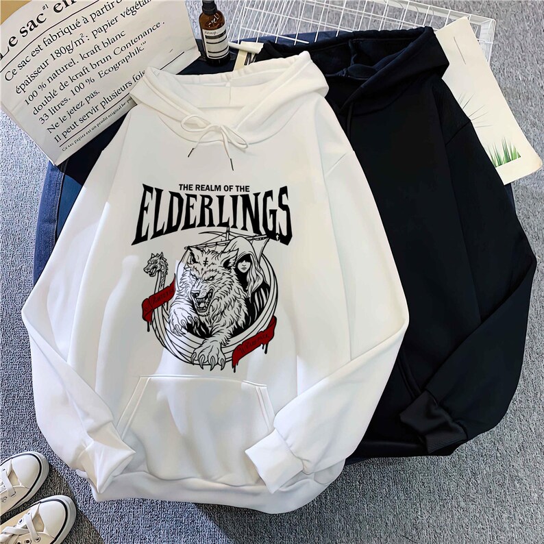 May include: White hoodie with a front pocket and drawstring. The graphic on the front features a wolf, the text "THE REALM OF THE ELDERLINGS", and other design elements. A black hoodie is next to it.