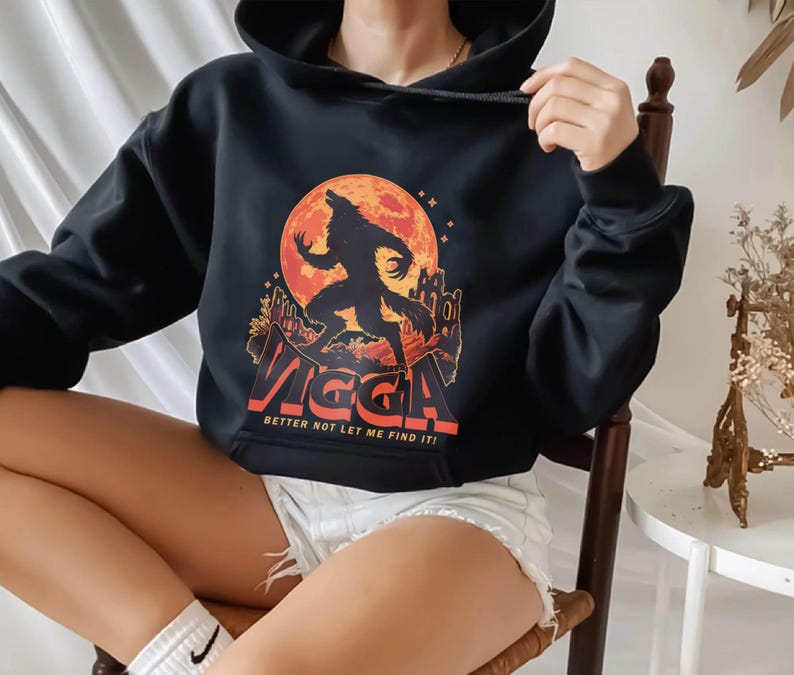 May include: Black hooded sweatshirt featuring a graphic of a howling werewolf against a full moon. The design includes the word "VIGGA" in orange and the text "BETTER NOT LET ME FIND IT!" This apparel is perfect for fans of horror and fantasy.