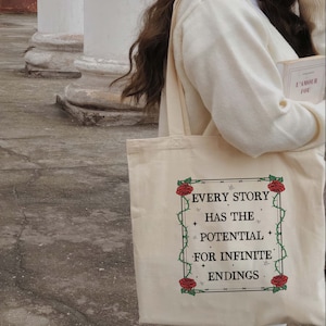 May include: A white canvas tote bag with a floral design and the text "Every story has the potential for infinite endings".