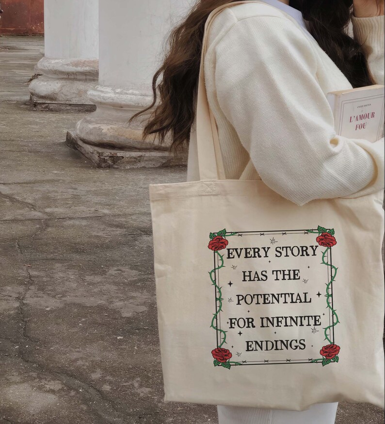 May include: A white canvas tote bag with a floral design and the text "Every story has the potential for infinite endings".