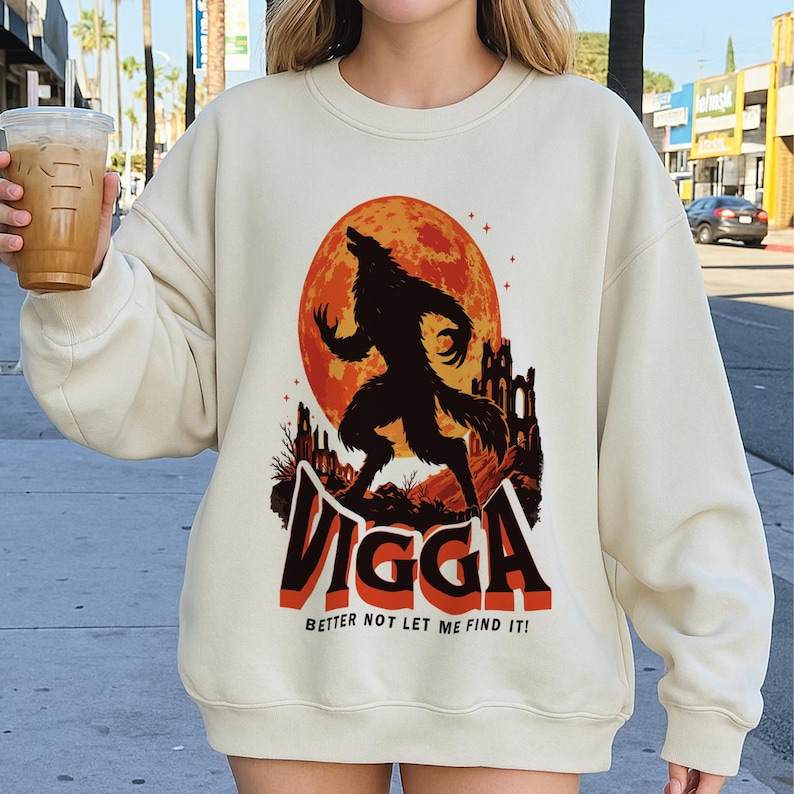 May include: Cream-colored sweatshirt featuring a graphic of a howling werewolf against a full orange moon. The design includes the word "Vigga" in bold, black and red letters, with the phrase "Better not let me find it!" below.