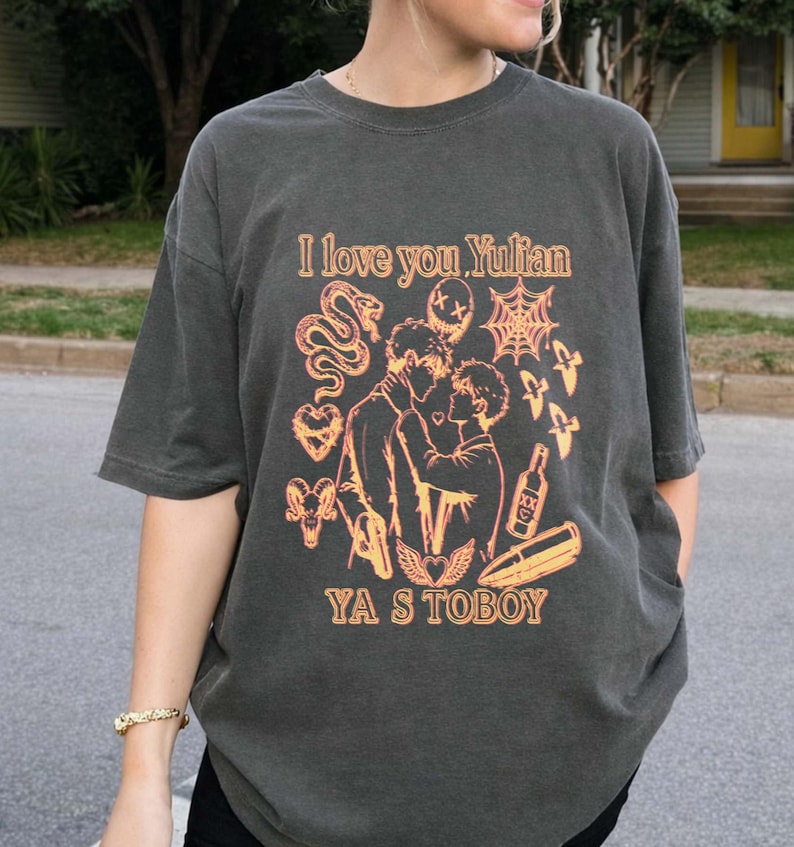 May include: Dark gray t-shirt with the text "I love you Yulian" above a graphic of two people embracing, with additional illustrations. The text "YA S TOBOY" is printed below the graphic.
