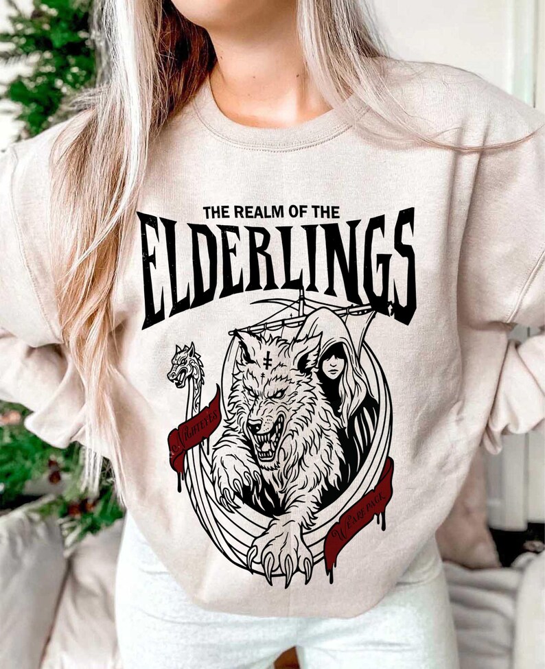 May include: Beige sweatshirt with a black and red graphic. The graphic features a wolf, a woman, and the text "THE REALM OF THE ELDERLINGS". A banner reads "WOLF PACK".
