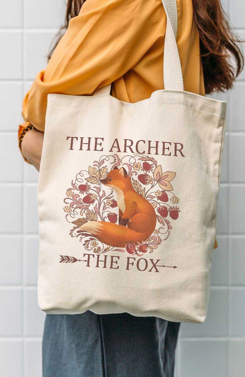 May include: A beige canvas tote bag with a fox illustration and the text "The Archer The Fox".