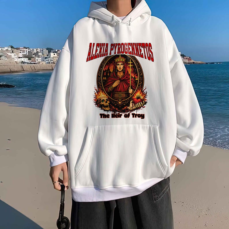 Op de afbeelding: Witte hoodie met een voorzak en een grafisch ontwerp. Het ontwerp toont de tekst "ALEXIA PYROGENNETOS" boven een cirkelvormige afbeelding van een persoon in een rode jurk die een kruis vasthoudt, met de tekst "The Heir of Troy" eronder.