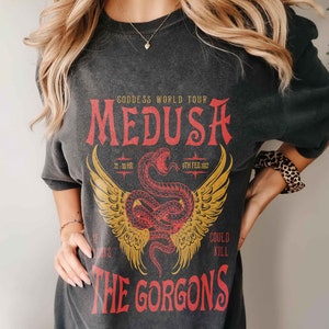 K&ouml;nnte beinhalten: Schwarzes T-Shirt mit einem grafischen Druck einer roten Schlange mit Fl&uuml;geln und dem Text "Goddess World Tour Medusa 22.00 HR 9TH FEB. 1982 The Gorgons Could Kill"