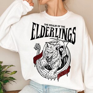 May include: White sweatshirt with a black and red graphic. The graphic features a wolf, a woman, and a Viking ship with the text "THE REALM OF THE ELDERLINGS". A red banner with text is also included.