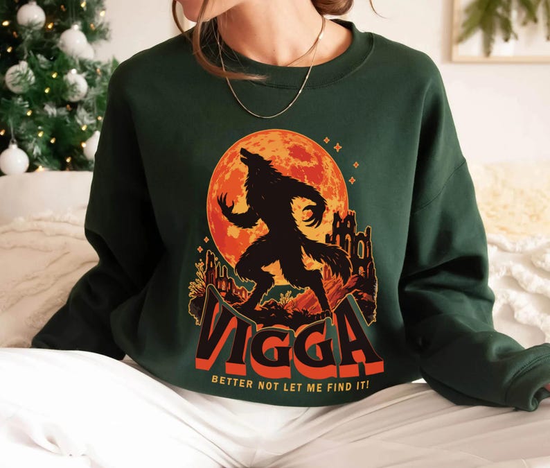 May include: Dark green sweatshirt featuring a graphic of a werewolf against a red moon and a castle silhouette. The word "Vigga" is displayed in orange and white, with the text "Better not let me find it!" below.