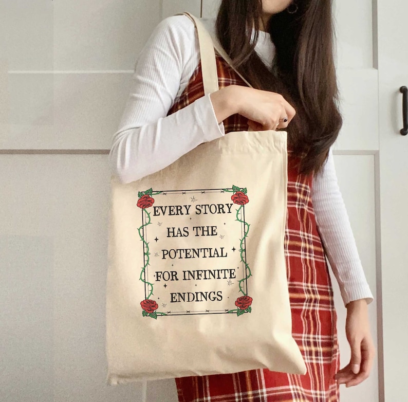 May include: A beige tote bag with a black and white graphic that reads "Every story has the potential for infinite endings". The graphic is surrounded by a black border and red roses with green vines.