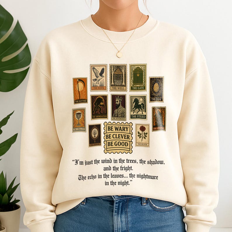 May include: Cream-colored sweatshirt with a collection of vintage-style postage stamp graphics. The stamps feature various illustrations and text, including the phrases "BE WARY BE CLEVER BE GOOD" and a quote about wind and trees.