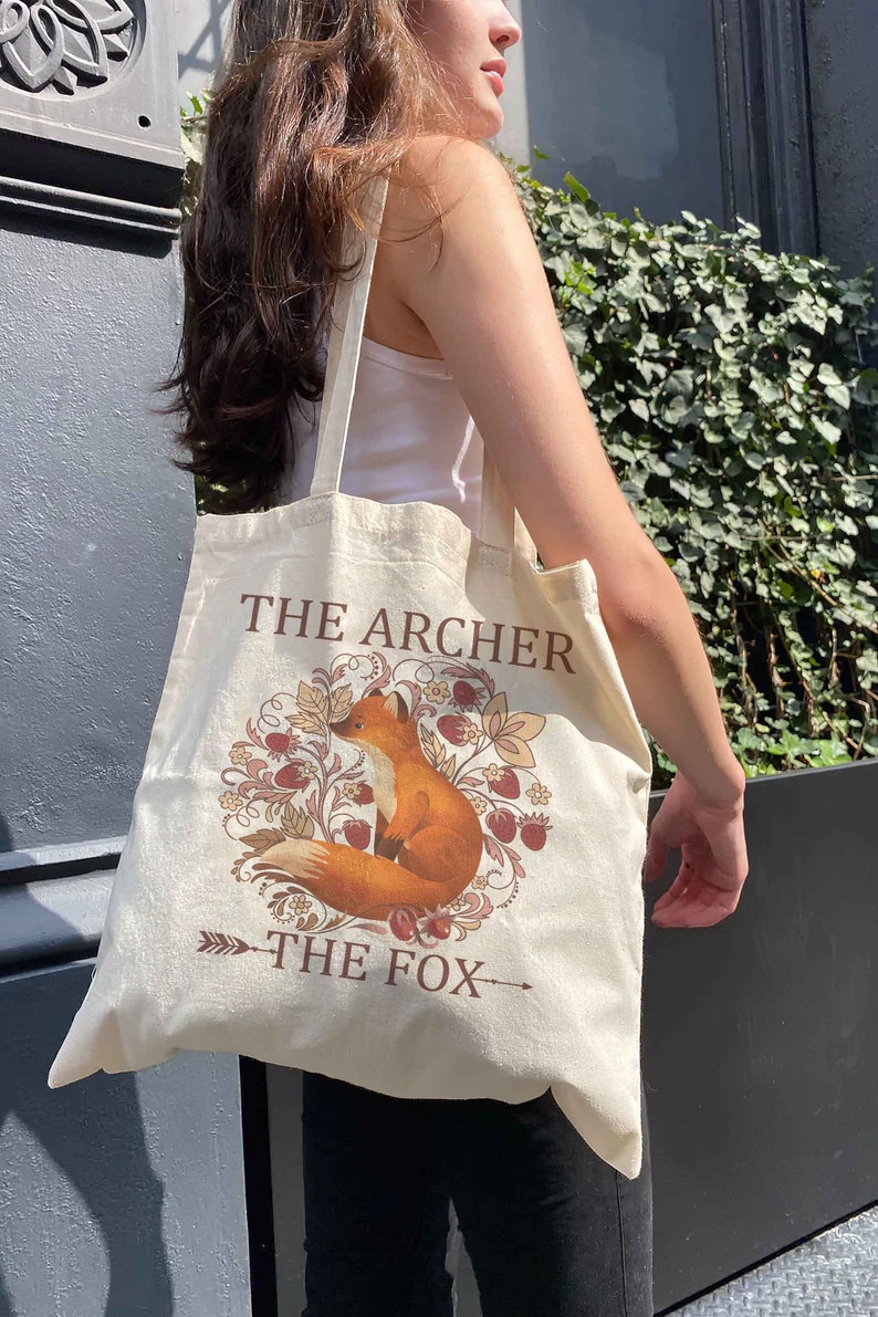 May include: A beige tote bag with a fox illustration and the text "The Archer The Fox".