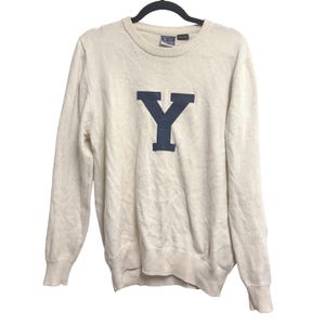 May include: A cream-colored long-sleeve knit sweater featuring a large navy blue letter Y centered on the chest. The garment has a ribbed crew neckline, ribbed cuffs, and a ribbed hem. A small tag is visible at the inner neck collar area.