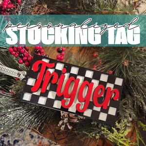 May include: A black and white checkered stocking tag with the name "Trigger" written in red letters.